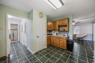 Kitchen featuring brown cabinetry, dark tile patterned flooring, baseboards, light countertops, and a textured ceiling