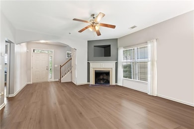 Unfurnished living room featuring arched walkways, wood finished floors, ceiling fan, stairs, and a fireplace