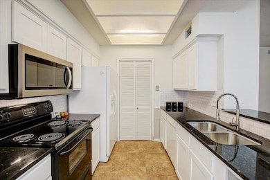 Kitchen with black range with electric stovetop, dark stone countertops, tasteful backsplash, stainless steel microwave, and white cabinets