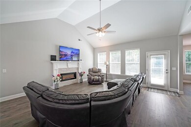Living area with vaulted ceiling, ceiling fan, a glass covered fireplace, dark wood finished floors, and baseboards