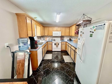 Kitchen featuring white appliances, dark marble finish floors, a textured ceiling, light countertops, and light brown cabinetry