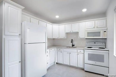 Kitchen featuring white appliances, light countertops, white cabinetry, decorative backsplash, and recessed lighting