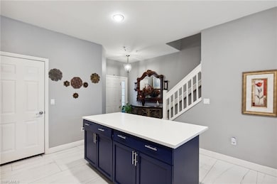 Kitchen with blue cabinetry, light marble finish flooring, baseboards, and light countertops
