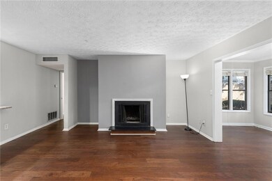 Unfurnished living room featuring wood finished floors, a fireplace with raised hearth, baseboards, and a textured ceiling