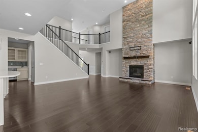 Unfurnished living room with recessed lighting, dark wood-type flooring, a towering ceiling, a stone fireplace, and stairway