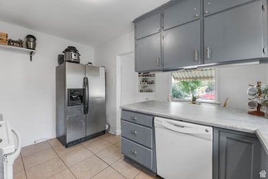 Kitchen with gray cabinetry, white appliances, light countertops, and light tile patterned floors