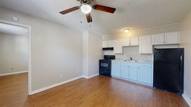Kitchen with black appliances, a textured ceiling, dark wood finished floors, white cabinetry, and a ceiling fan