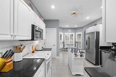 Kitchen with appliances with stainless steel finishes, backsplash, white cabinets, a ceiling fan, and dark stone countertops