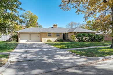 Single story home featuring a chimney, driveway, a garage, a shingled roof, and brick siding