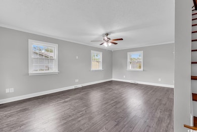 Empty room featuring crown molding, a textured ceiling, ceiling fan, dark wood-style floors, and stairs