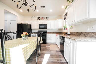 Kitchen with black appliances, white cabinets, wood-style floors, recessed lighting, and light stone counters