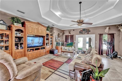 Living area with light tile patterned floors, a ceiling fan, visible vents, french doors, and a raised ceiling