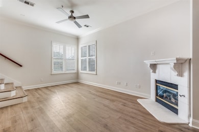 Unfurnished living room featuring crown molding, stairs, a tiled fireplace, wood finished floors, and a ceiling fan