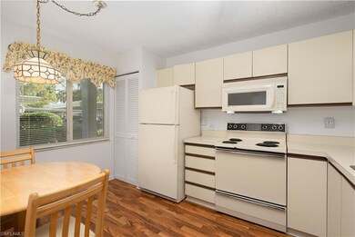 Kitchen with cream cabinets, white appliances, dark wood-type flooring, light countertops, and decorative light fixtures