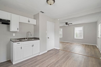 Kitchen featuring light wood finished floors, dark countertops, white cabinets, a ceiling fan, and custom range hood