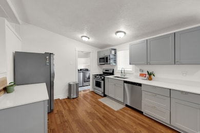 Kitchen with gray cabinets, stainless steel appliances, a textured ceiling, light wood-style floors, and washing machine and clothes dryer