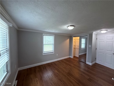Unfurnished bedroom featuring dark wood-style floors, a textured ceiling, ornamental molding, multiple windows, and a closet