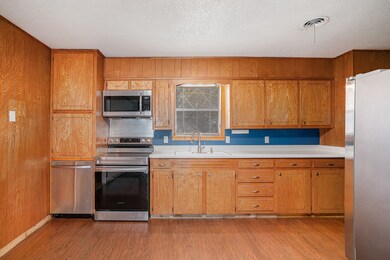 Kitchen featuring appliances with stainless steel finishes, light countertops, dark wood-style floors, a textured ceiling, and brown cabinets