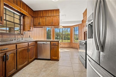 Kitchen featuring appliances with stainless steel finishes, brown cabinets, light tile flooring, a peninsula
