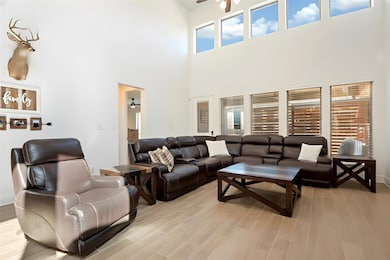 Living area with ceiling fan, light wood-style flooring, healthy amount of natural light, and a high ceiling