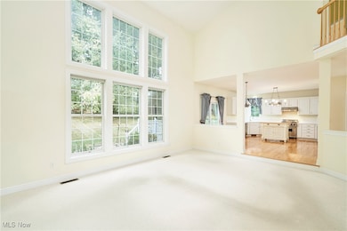 Unfurnished living room featuring light carpet, a chandelier, and a towering ceiling