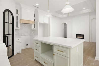 Kitchen with hanging light fixtures, light stone counters, decorative backsplash, a kitchen island, and white cabinetry