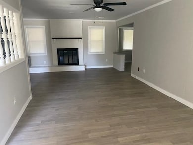 Unfurnished living room with a ceiling fan, baseboards, crown molding, a fireplace, and wood finished floors