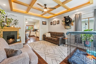 Living room with coffered ceiling, ceiling fan, wood finished floors, beamed ceiling, and a lit fireplace