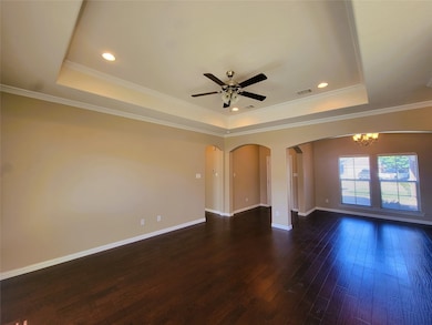 Spare room featuring a raised ceiling, dark wood-style flooring, arched walkways, ornamental molding, and a chandelier