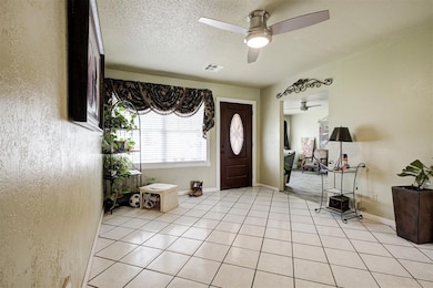 Foyer entrance with ceiling fan, a textured ceiling, light tile patterned flooring, and baseboards