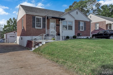 View of front facade with an outbuilding, brick siding, a front yard, a detached garage, and a shingled roof