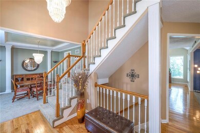 Staircase with a chandelier, wood finished floors, and ornamental molding