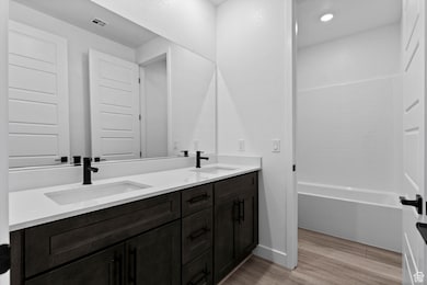 Full bathroom featuring double vanity, light wood-style floors, and shower / tub combination