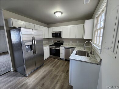 Kitchen featuring sink, hardwood / wood-style flooring, light stone countertops, stainless steel appliances, and white cabinetry