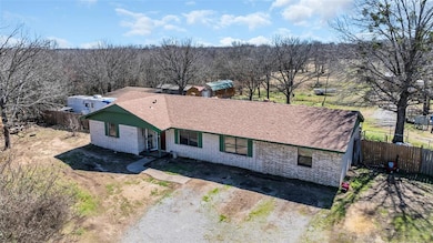 Single story home with brick siding, roof with shingles, and dirt driveway