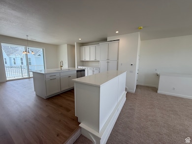 Kitchen featuring a center island with sink, a chandelier, dishwasher, white cabinetry, and light countertops