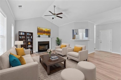 Living area with light wood-style flooring, a ceiling fan, a fireplace with raised hearth, baseboards, and vaulted ceiling