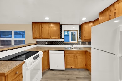 Kitchen with white appliances, decorative backsplash, light wood-type flooring, brown cabinets, and light countertops