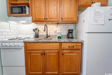 Kitchen with range hood, white appliances, tasteful backsplash, light stone counters, and a sink