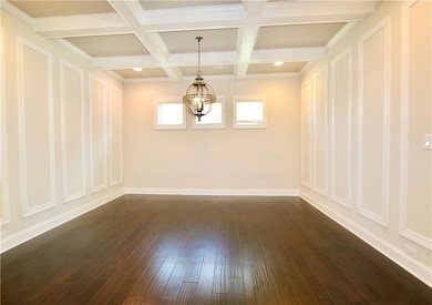 Spare room featuring a chandelier, beamed ceiling, dark hardwood / wood-style flooring, and coffered ceiling