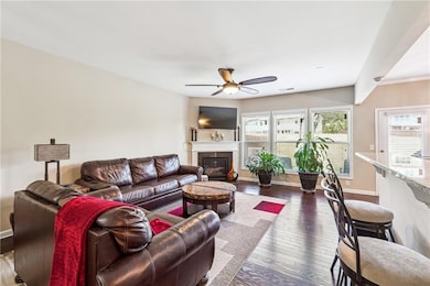 Living room featuring dark wood-type flooring, ceiling fan, a glass covered fireplace, and baseboards