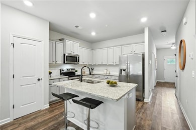 Kitchen featuring stainless steel appliances, dark wood-style floors, a kitchen island with sink, light stone counters, and a kitchen bar