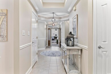 Hall with a raised ceiling, crown molding, and lig