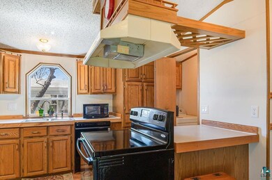 Kitchen with a sink, black appliances, under cabinet range hood, light countertops, and a textured ceiling