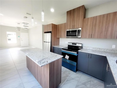 Kitchen featuring a kitchen island, stainless steel appliances, light stone counters, and pendant lighting