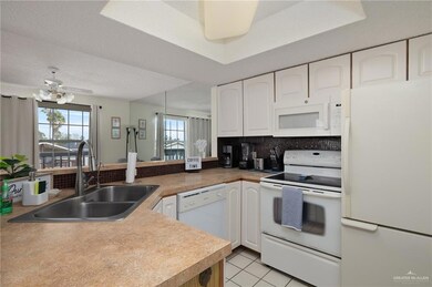 Kitchen with white appliances, tasteful backsplash, white cabinets, a peninsula, and a sink