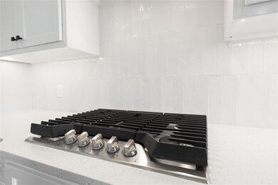 Kitchen view of stainless steel gas stovetop, light stone counters, white cabinetry, and decorative backsplash