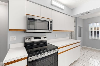 Kitchen featuring appliances with stainless steel finishes, a textured ceiling, light countertops, white cabinetry, and light tile patterned flooring