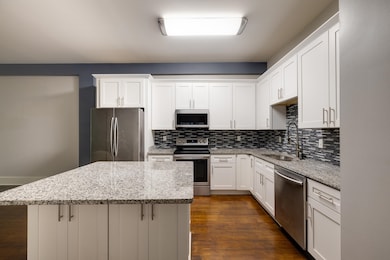 Kitchen featuring appliances with stainless steel finishes, a sink, a center island, backsplash, and white cabinetry