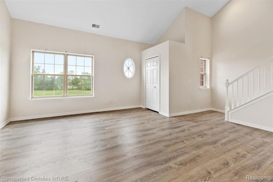Unfurnished living room featuring healthy amount of natural light, light wood-style floors, high vaulted ceiling, and stairway